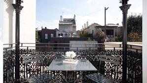 A balcony with a table and chairs, overlooking a street with buildings and a clear sky. - Perfect Located Comfy Studio With Balcony (Sydney)