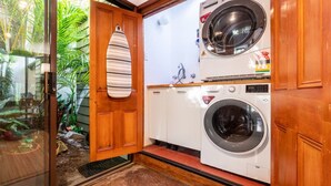 A compact laundry room with a washing machine and dryer, wooden cabinets, and a glass door leading to a garden.
