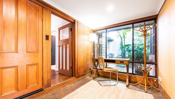 A wooden door, a desk with a chair, a window with a view of greenery, and a coat rack.