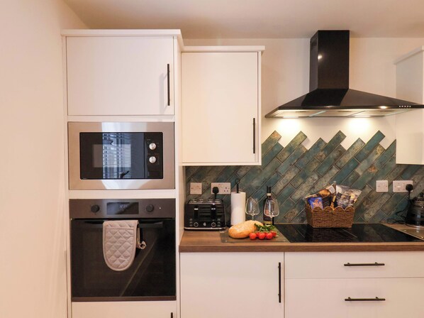 A modern kitchen with white cabinets, a black microwave, a built-in oven, and a stainless steel range hood. - Sandy Nook (Redcar)