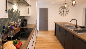A modern kitchen with a wooden countertop, a built-in stove, and a large island with a sink. There are hanging lights and a wall clock. - Sandy Nook (Redcar)