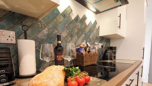 A kitchen counter with a loaf of bread, tomatoes, a bottle of wine, and a basket of snacks. - Sandy Nook (Redcar)