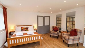 A bedroom with a wooden bed, two plaid armchairs, a small table with a bottle and glass, and a window with blinds. - Sandy Nook (Redcar)