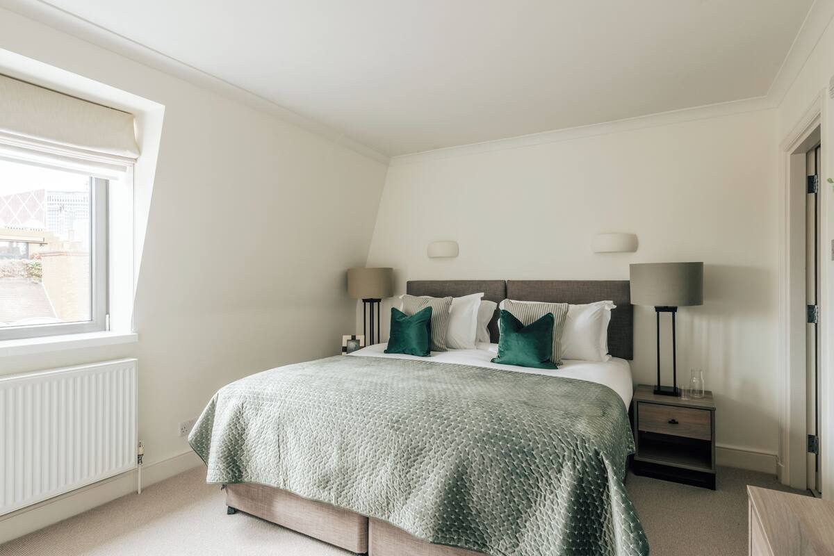 Une chambre à coucher avec un lit, deux tables de chevet, une fenêtre et un radiateur.