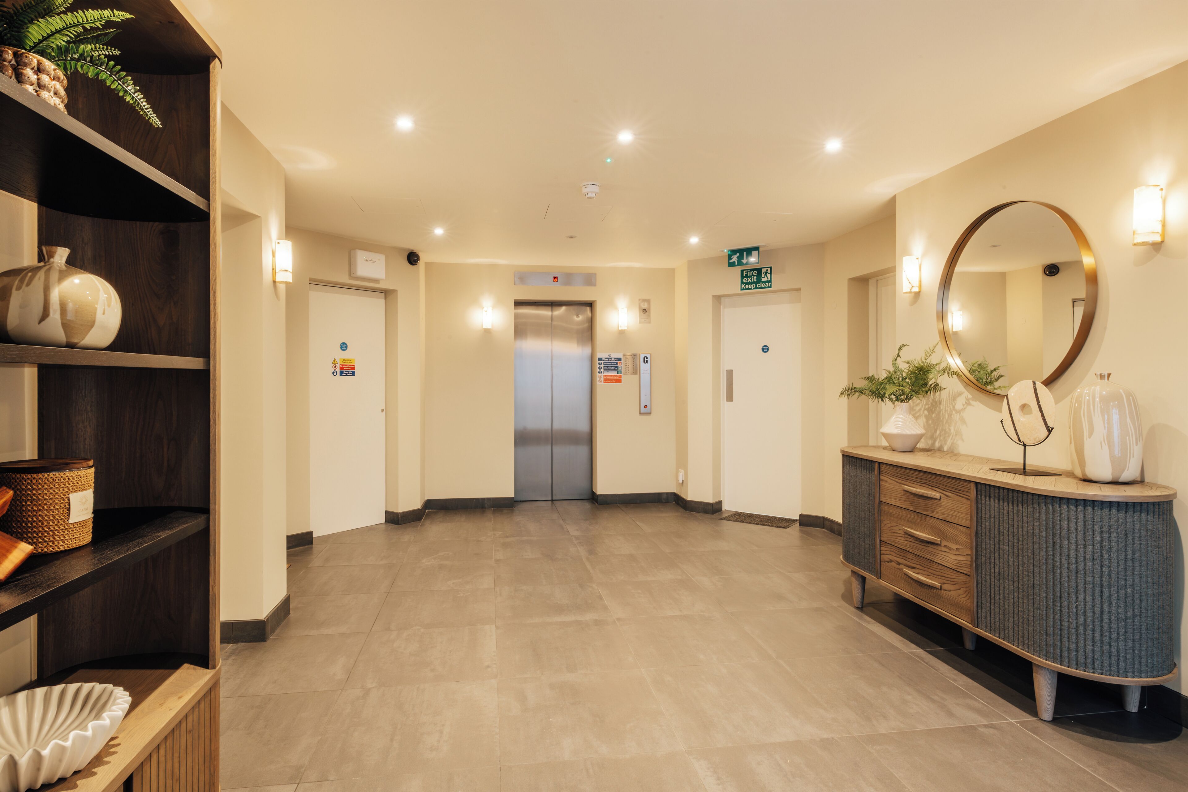 A hotel lobby with a reception desk, a large mirror, and an elevator.