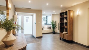 A modern hotel lobby with a reception desk, a wooden display cabinet, and a seating area with a view of the outdoors.