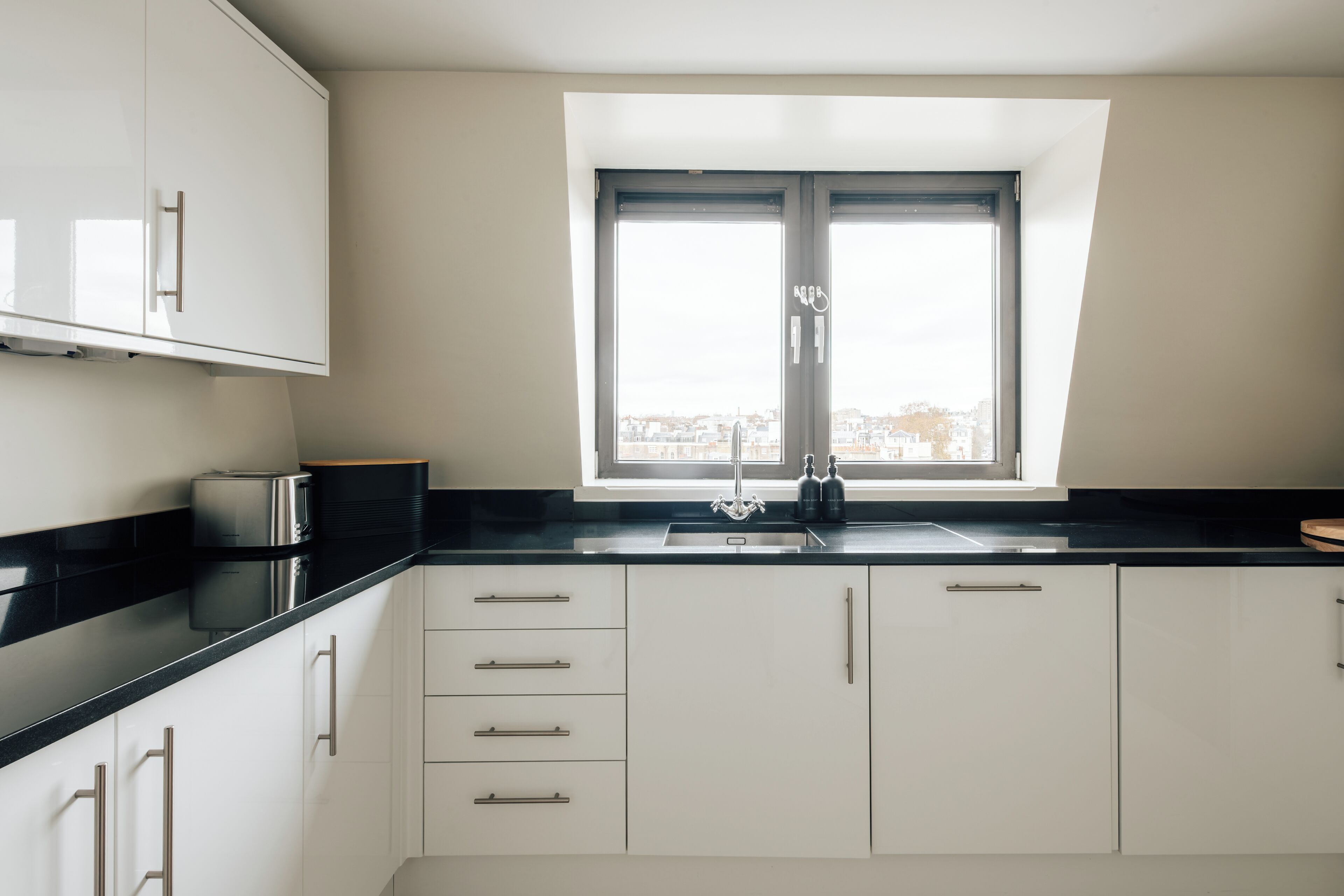 A modern kitchen with white cabinets, a black countertop, and a window with a view of the city.