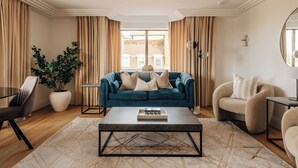 A living room with a blue sofa, beige armchairs, a coffee table, and a large window with curtains.
