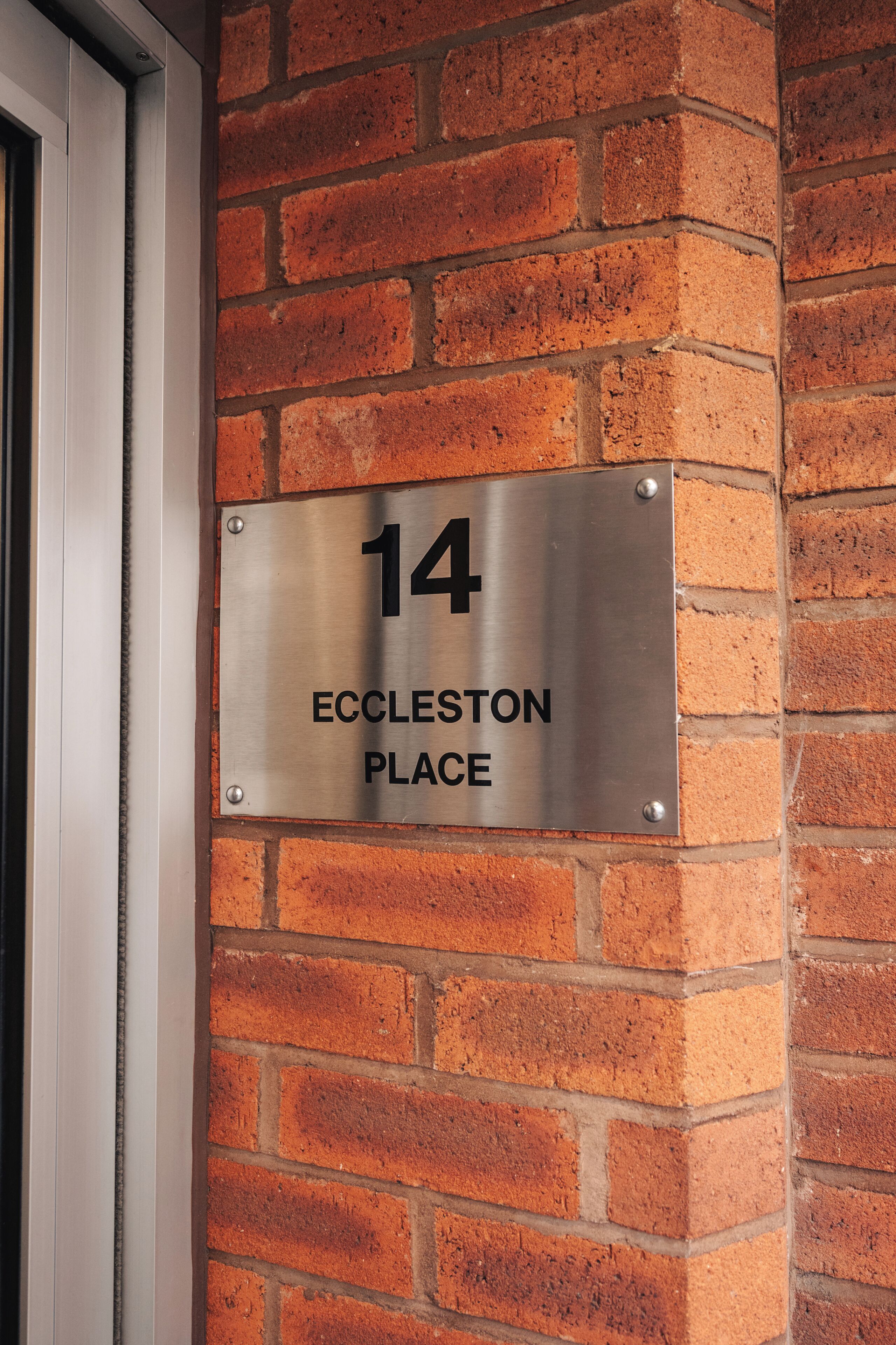 Eine Metallplatte mit der Nummer 14 und der Aufschrift 'Eccleseston Place' ist an einer Backsteinmauer angebracht.