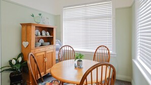 Un comedor con mesa y sillas de madera, un armario con vajilla y una ventana con persianas.
