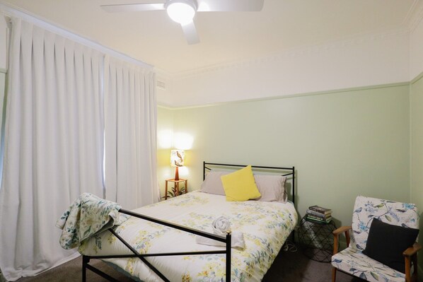 Une chambre à coucher avec un lit, une chaise, une table de chevet avec une lampe et une fenêtre avec des rideaux.