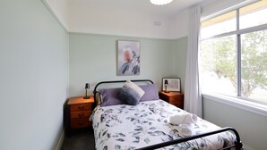 Un dormitorio con cama, mesita de noche, lámpara, ventana con vistas a árboles y luz en el techo.