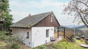 A small, single-story house with a sloped roof, a wooden deck, and a garden area. - Cozy Kirschallee Cottage with Mountain View, Private Terrace & Shared Garden (Hohnstein)