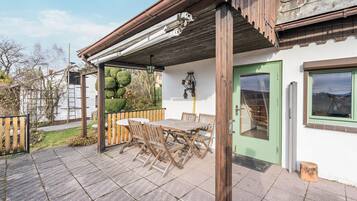 A patio with a wooden table and chairs, a green door, and a white wall with a window.