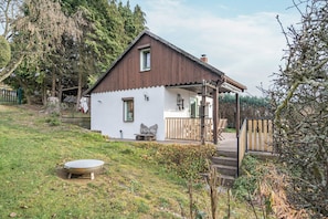 A small house with a porch, a stone bench, and a wooden fence. - Cozy Kirschallee Cottage with Mountain View, Private Terrace & Shared Garden (Hohnstein)