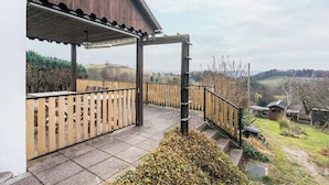 A covered outdoor area with a wooden deck, a metal railing, and a view of the countryside. - Cozy Kirschallee Cottage with Mountain View, Private Terrace & Shared Garden (Hohnstein)
