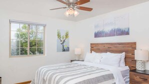 Habitació amb llit, ventilador de sostre, finestra i decoració a les parets.
