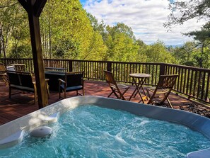 A hot tub on a wooden deck with outdoor furniture and a view of trees.