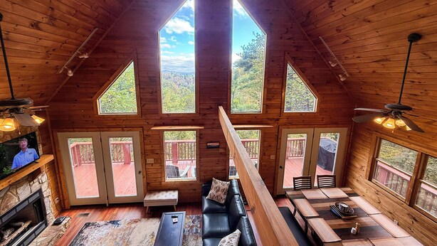 A spacious loft-style room with a high ceiling, large windows, a fireplace, a sofa, and a dining area. - Mountaintop Memories-Hot Tub, Game Room, Pet Friendly, Near Grayson Highlands (Grassy Creek)
