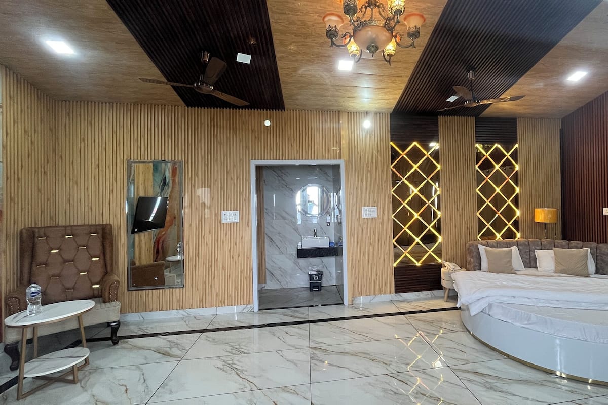 A hotel room with a large bed, a small table, a chair, a mirror, a vanity with a sink, and a chandelier.