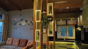 Uma sala de estar moderna com um sofá, arte decorativa nas paredes e uma cozinha com armários verdes e uma janela.