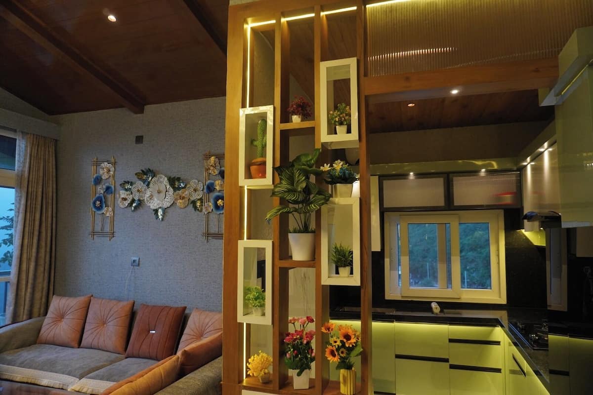 A modern living room with a sofa, decorative wall art, and a kitchen with green cabinets and a window.