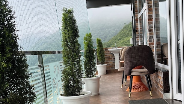 Varanda com vasos de plantas, uma cadeira e vista para uma paisagem montanhosa.