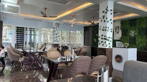 Interior moderno de restaurante com pé-direito alto, iluminação pendente e parede verde com plantas trepadeiras.