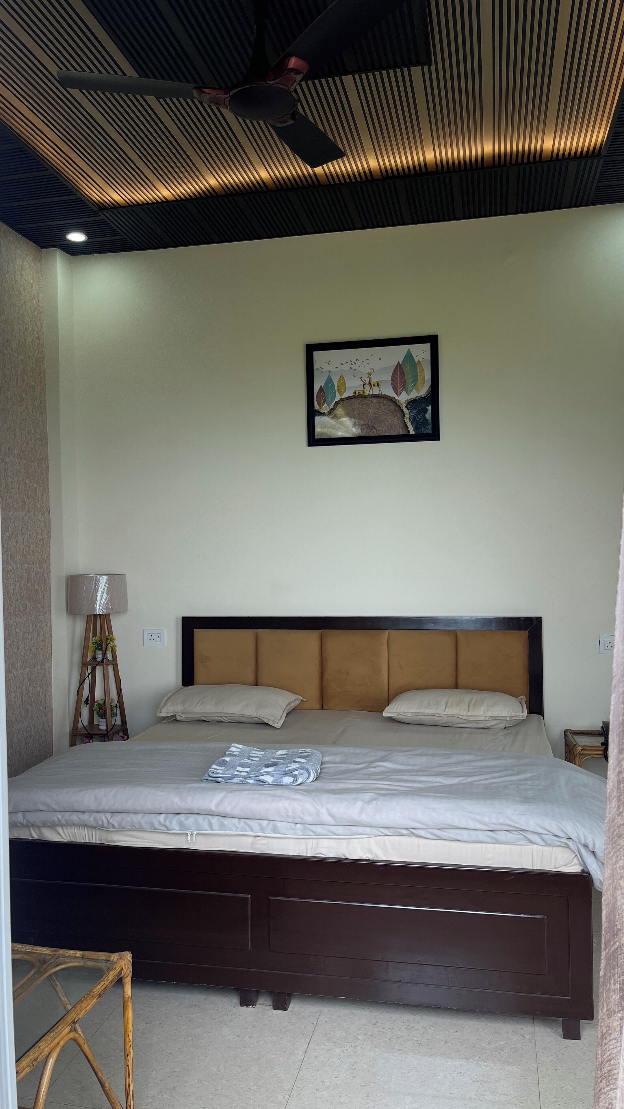 A bedroom with a bed, a headboard, a wall-mounted artwork, a floor lamp, and a bedside table.