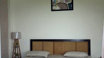 A bedroom with a bed, a headboard, a wall-mounted artwork, a floor lamp, and a bedside table.