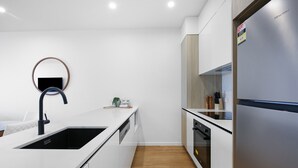 A modern kitchen with white cabinetry, a stainless steel refrigerator, and a black sink. - Surfers Paradise 2-bed Flat With Luxury Amenities (Gold Coast)
