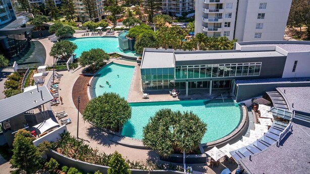 Um resort com várias piscinas, área coberta e edifícios altos ao fundo.