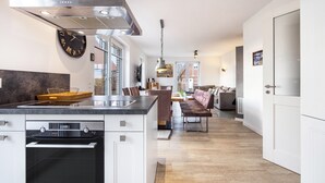 A modern kitchen with a built-in oven, a dining area with a bench, and a living room with a sofa. - Holiday Home 'Treibholz' with Private Terrace, Private Garden and Wi-Fi (Dassow)