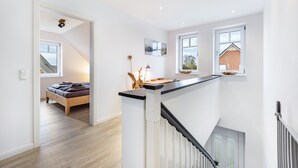 A modern interior with a staircase, a bed, and a view of a brick house through a window. - Holiday Home 'Treibholz' with Private Terrace, Private Garden and Wi-Fi (Dassow)