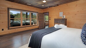 A wooden cabin bedroom with a large window, a bed, a ceiling fan, and a wooden dresser. - Great Trails Lodge - Blue Ridge (Epworth)