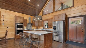 A spacious kitchen with wooden cabinetry, stainless steel appliances, and a large island with bar stools. - Great Trails Lodge - Blue Ridge (Epworth)