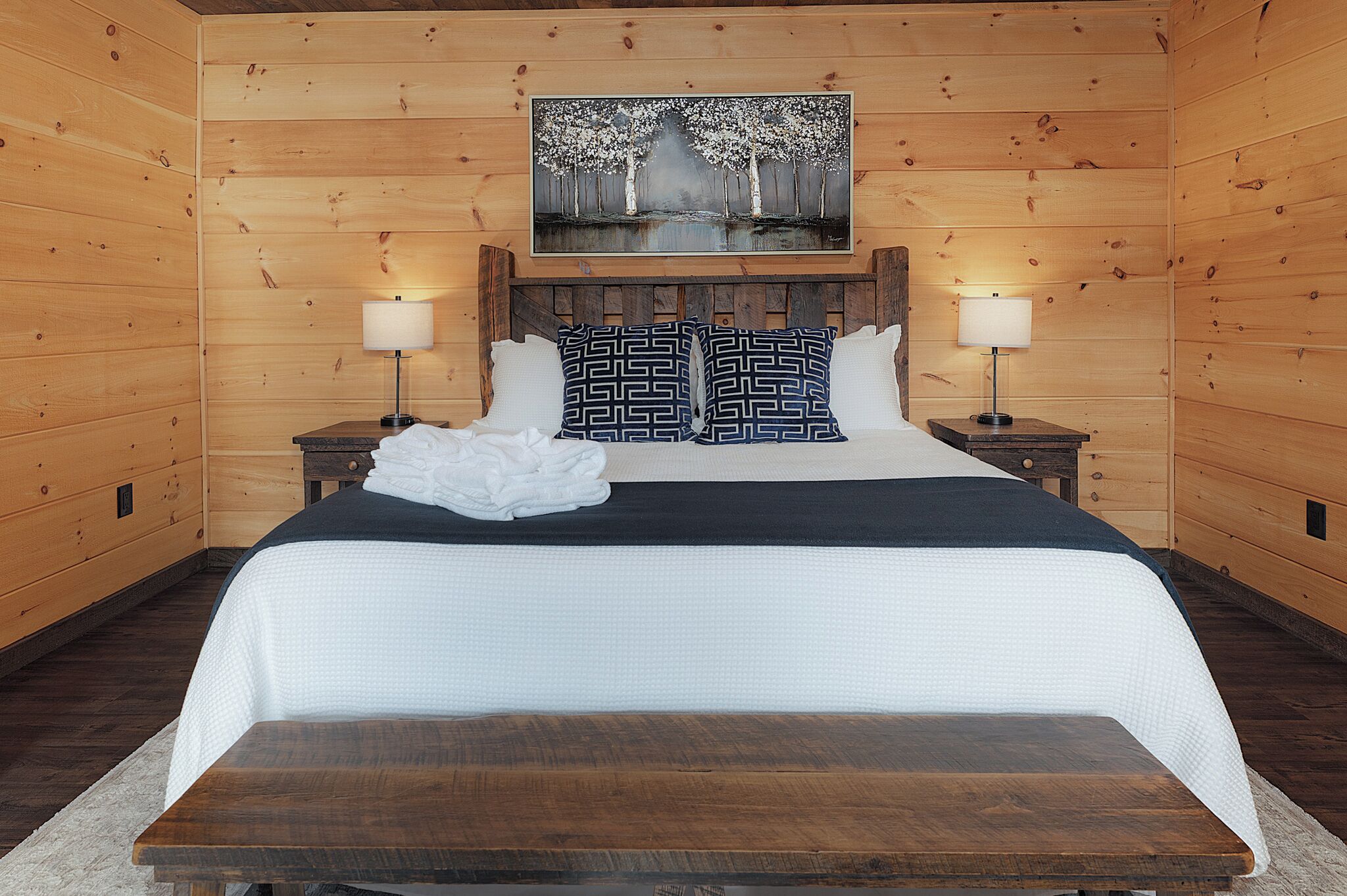 A wooden-paneled bedroom with a large bed, two nightstands, and a painting above the bed.