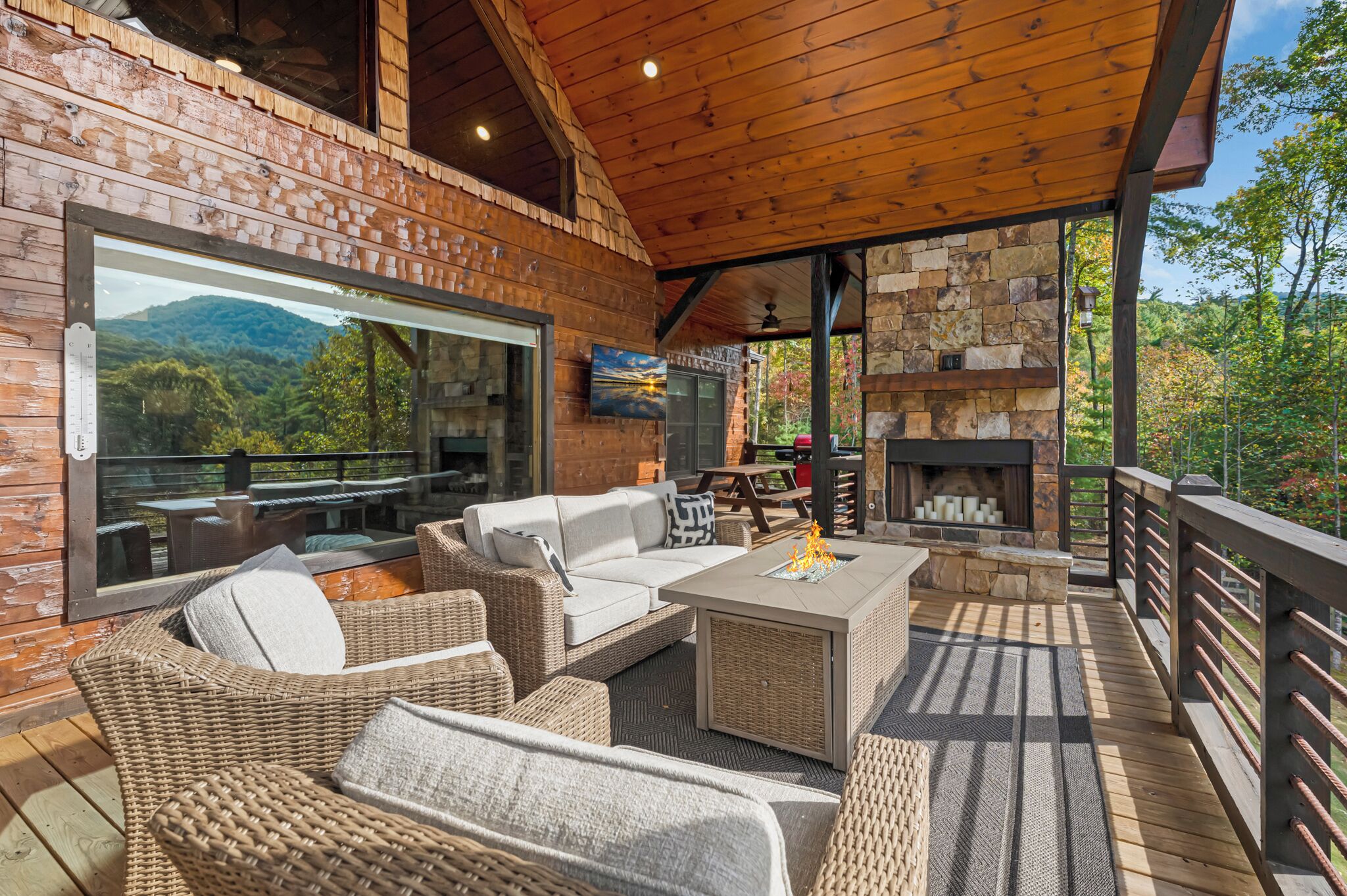 A wooden deck with wicker furniture, a stone fireplace, and a large window overlooking a mountainous landscape.