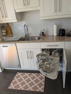 A modern kitchen with white cabinets, a stainless steel sink, and a dish rack. There are three pots under the counter and a coffee maker on the countertop. - Vibrant Upscale Kanata Retreat - Perfect for Families & Business Professionals (Ottawa)