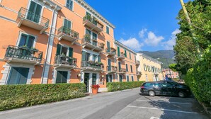 Une rangée d’immeubles à plusieurs étages dotés de balcons, une voiture garée et un ciel bleu dégagé.