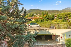 A parking area with a white car, surrounded by greenery and a mountainous backdrop. - Bogliaco Lake Front (Gargnano)