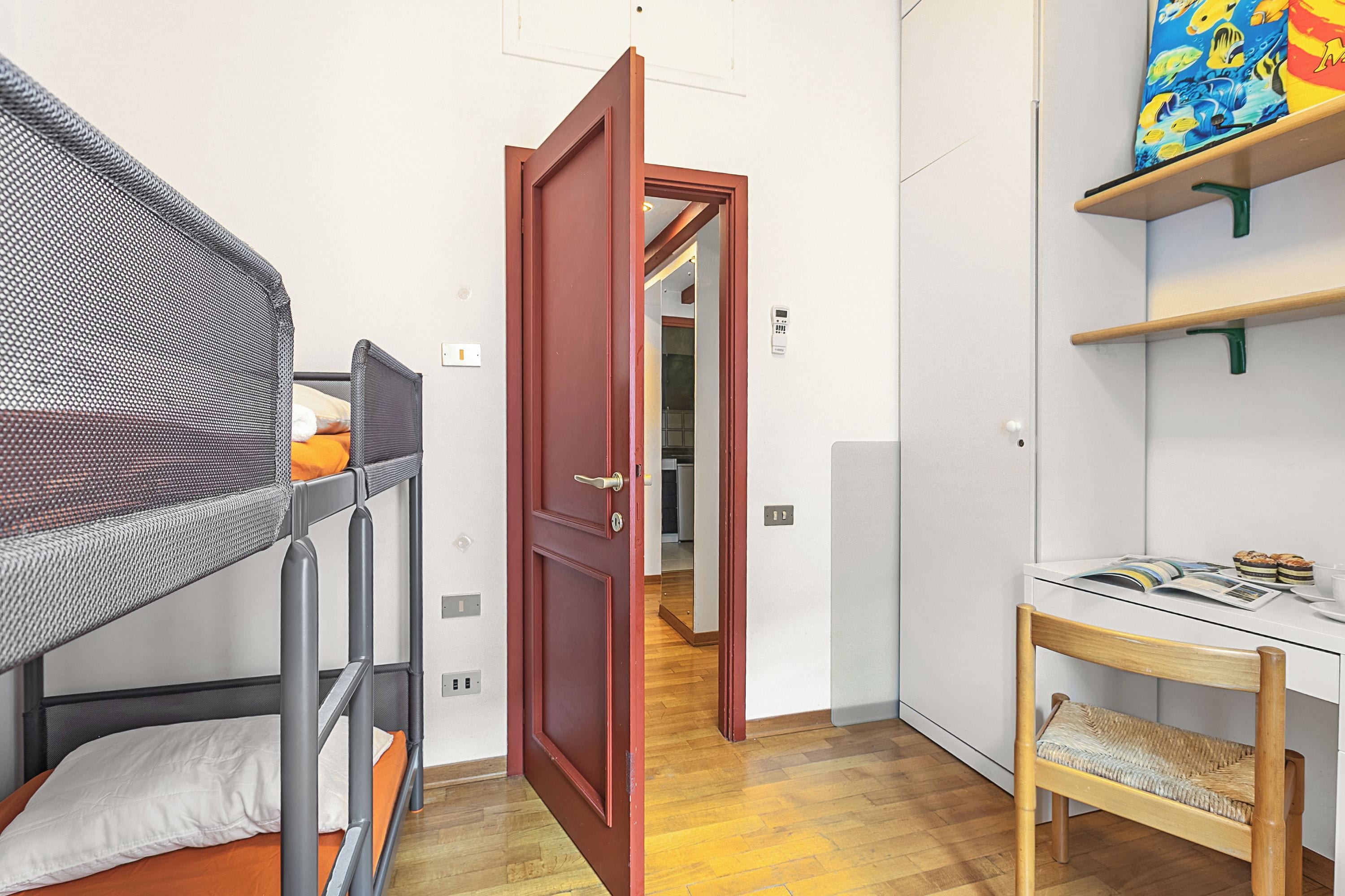 Una habitación pequeña con literas, un escritorio de madera y una puerta que da a otra habitación.
