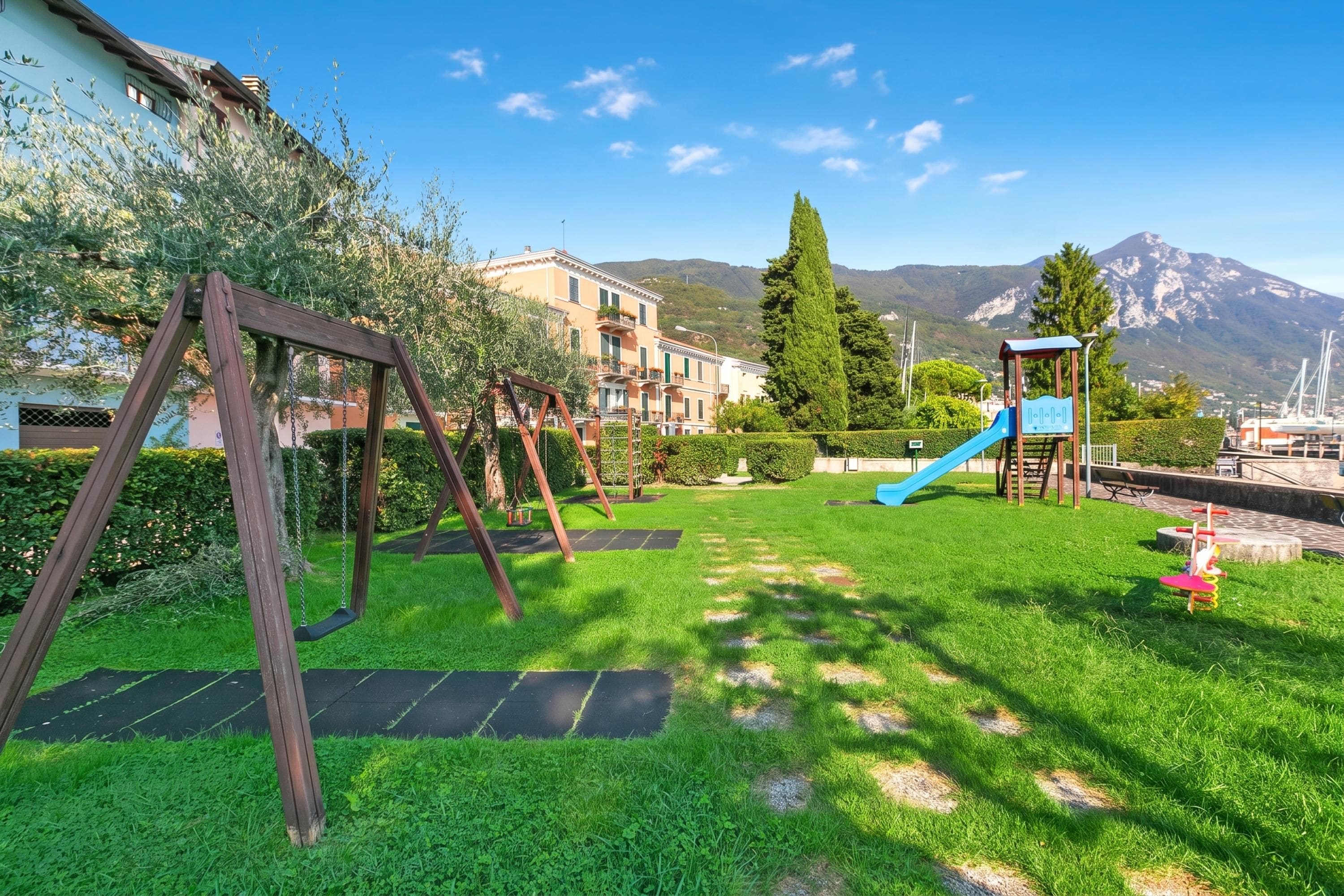 A playground with swings and a slide, surrounded by well-maintained grass and a view of mountains.