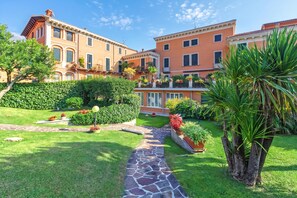 A courtyard with a stone pathway, lush greenery, and a building with multiple balconies. - Bogliaco Lake Front (Gargnano)