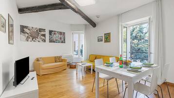 Ein modernes Wohnzimmer mit einer Couch, einem Esstisch mit Stühlen, einem Flachbildfernseher und Kunstwerken an den Wänden.