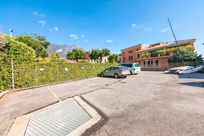 A parking area with cars, a building with a tiled roof, and a mountain in the background. - Bogliaco Lake Front (Gargnano)