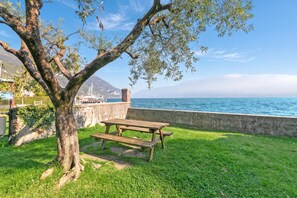 A picnic table and bench in a grassy area with a view of the sea and mountains in the background. - Bogliaco Lake Front (Gargnano)