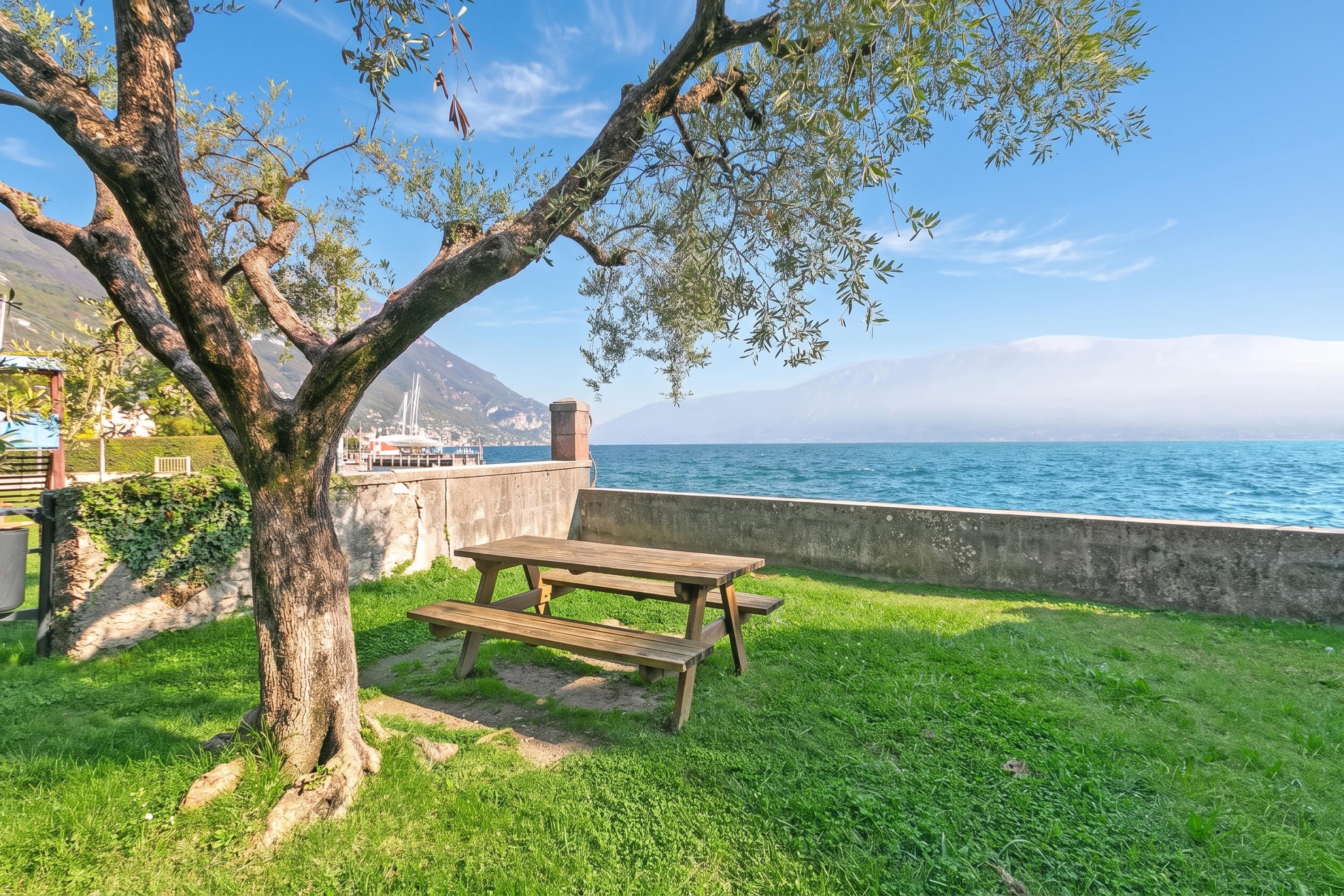 A picnic table and bench in a grassy area with a view of the sea and mountains in the background.