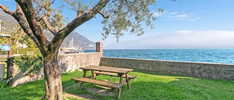 A picnic table and bench in a grassy area with a view of the sea and mountains in the background.