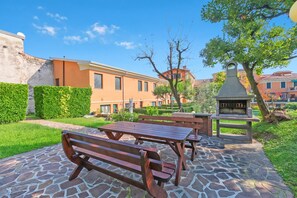 An outdoor patio with stone flooring, wooden benches, and a barbecue grill. - Bogliaco Lake Front (Gargnano)